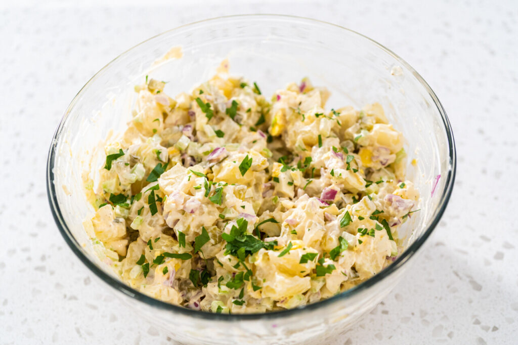 Mixing ingredients in a large glass mixing bowl to make potato salad.