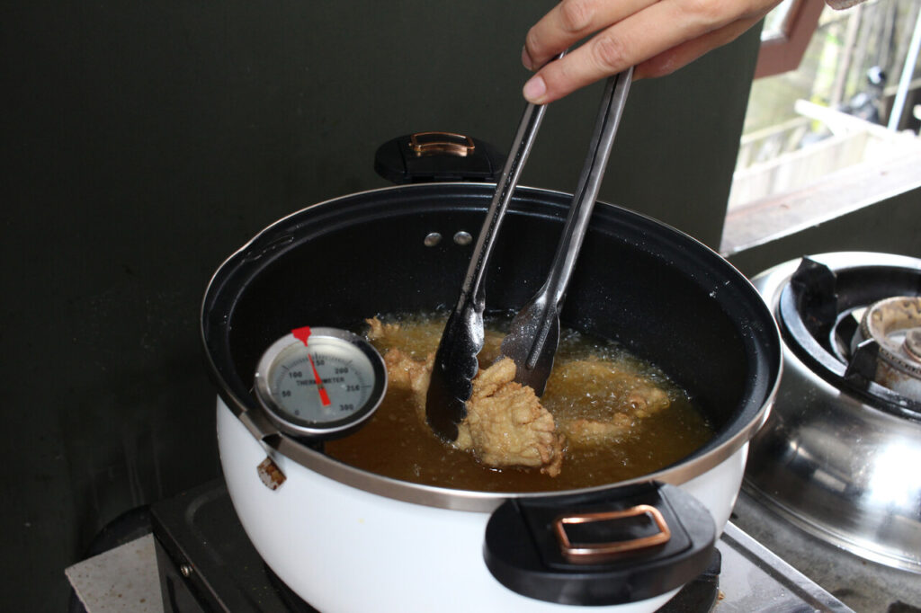 A frying pot with a thermometer showing precise oil temperature while chicken fries inside.