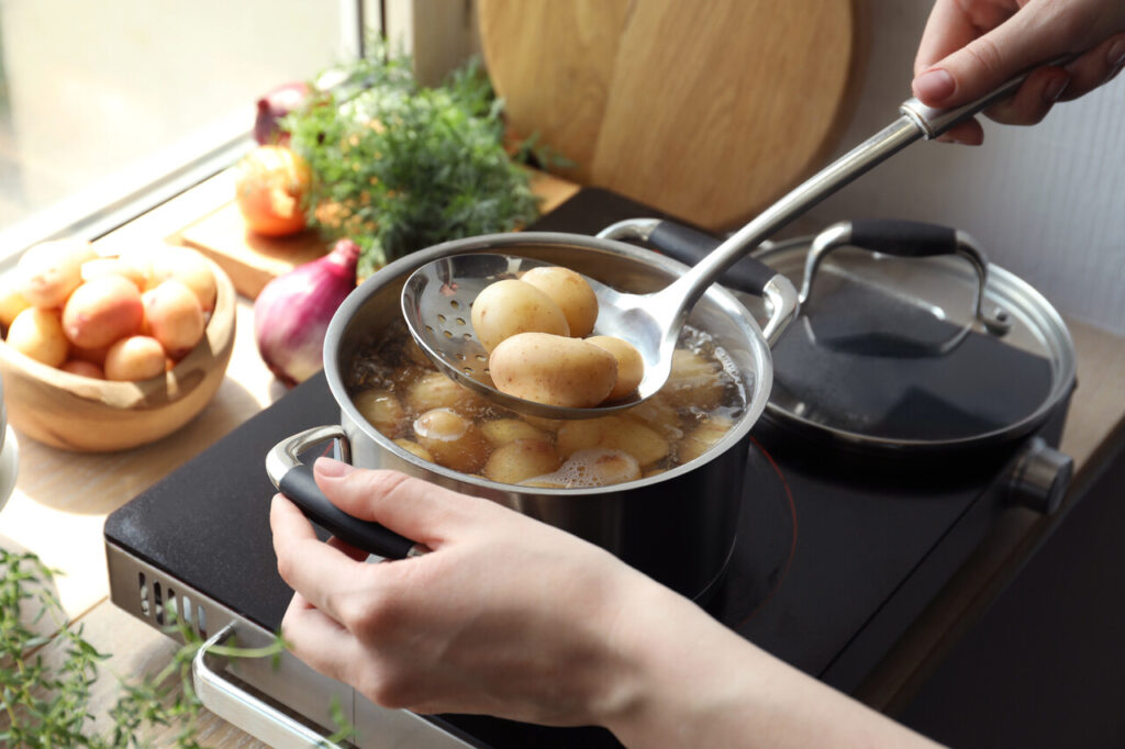 Woman taking boiled potato from pot on stove