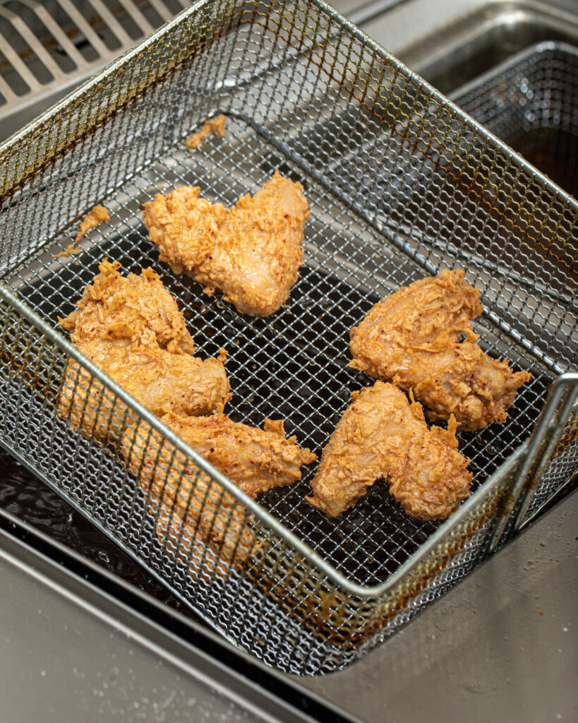 A close-up of fresh fried chicken under a heat lamp in a fast-food kitchen.