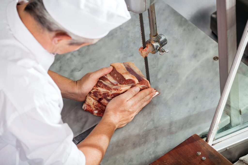 A butcher slicing or handling raw ribs on a wooden block