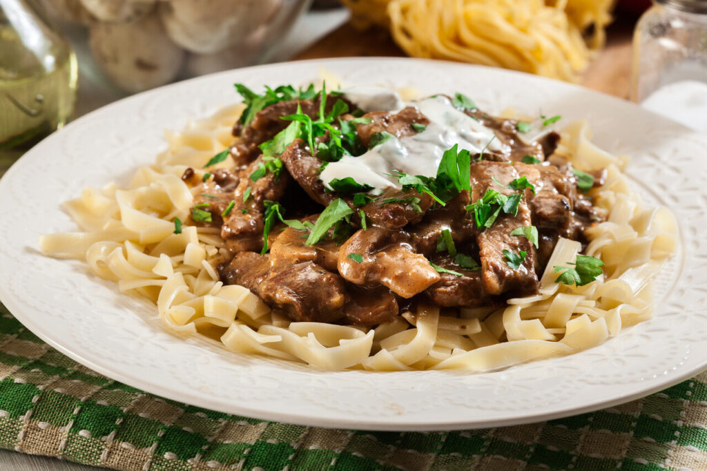 A steaming bowl of Beef Stroganoff served over egg noodles with fresh parsley