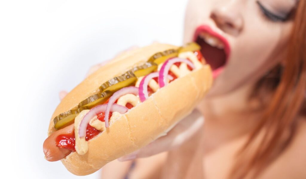 Beautiful sexy woman eating hot dog isolated on white background