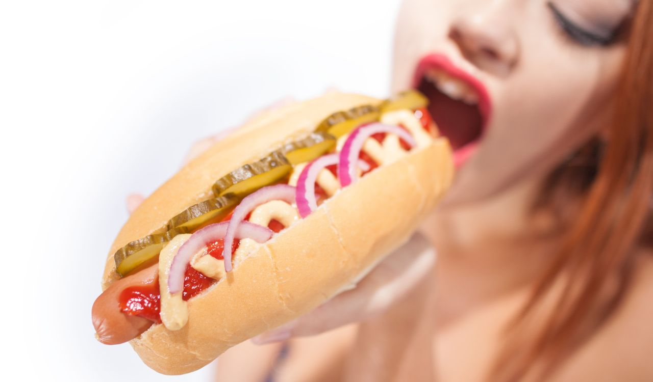 Beautiful sexy woman eating hot dog isolated on white background
