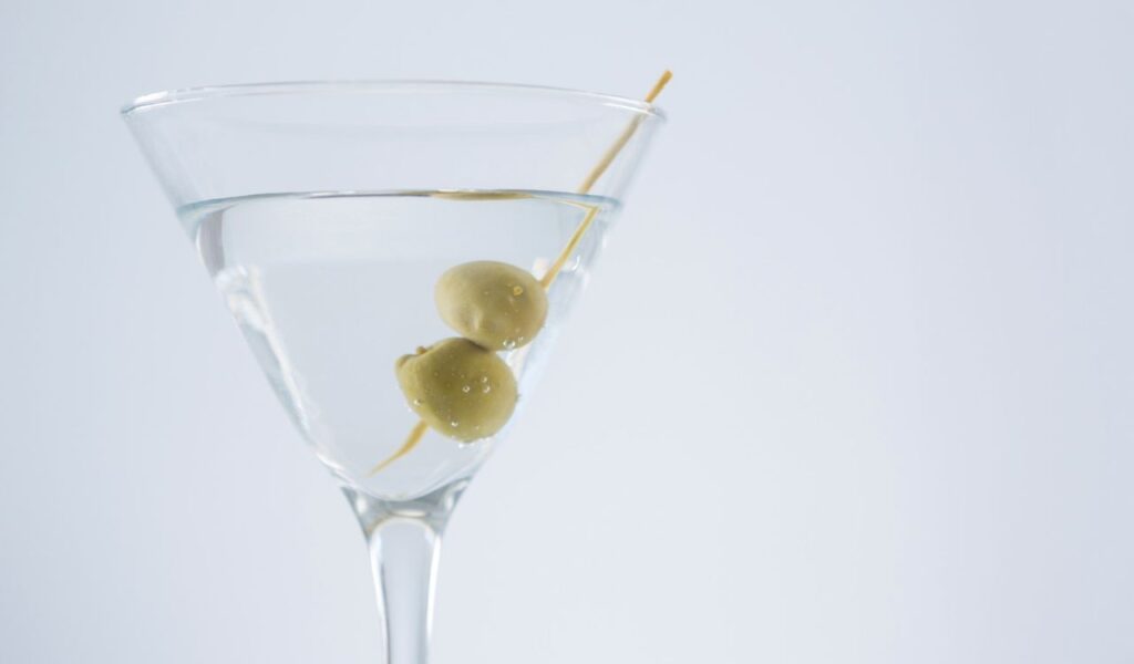 Close-up of cocktail martini with olives on table against white background