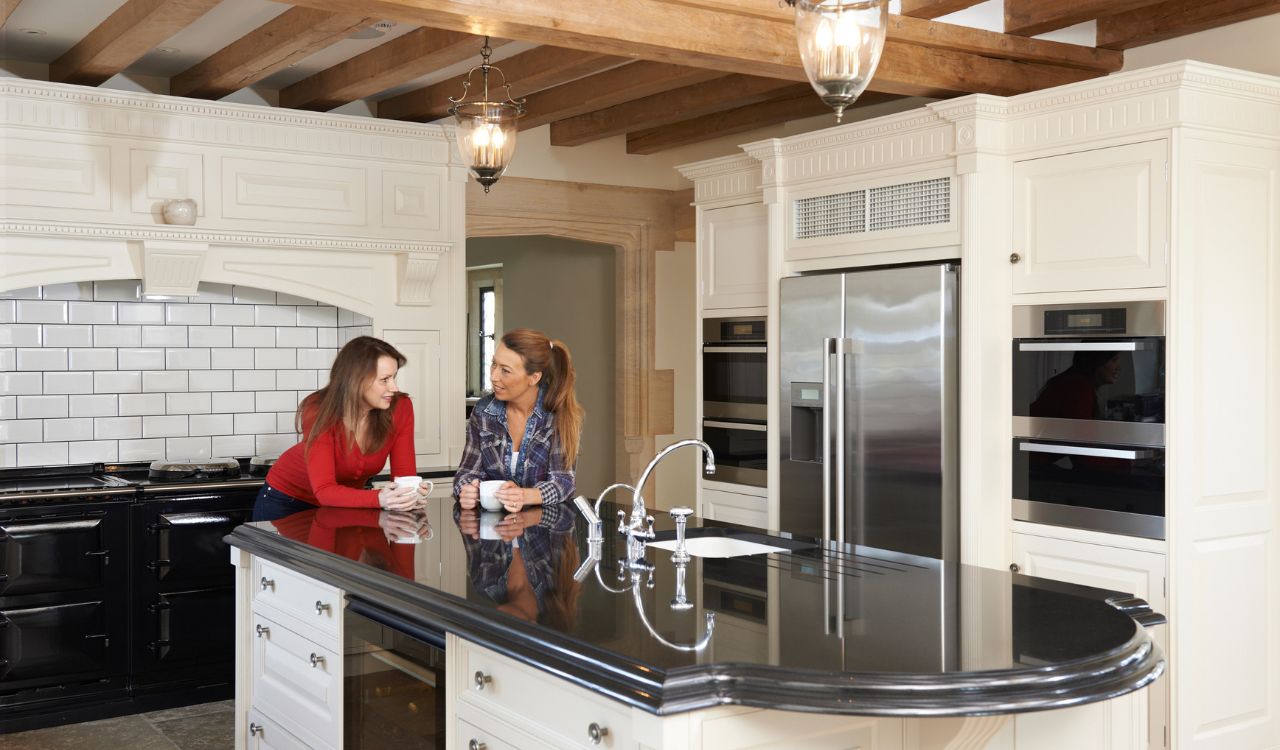 Mature Female Friends Standing In New Luxury Fitted Kitchen And Talking