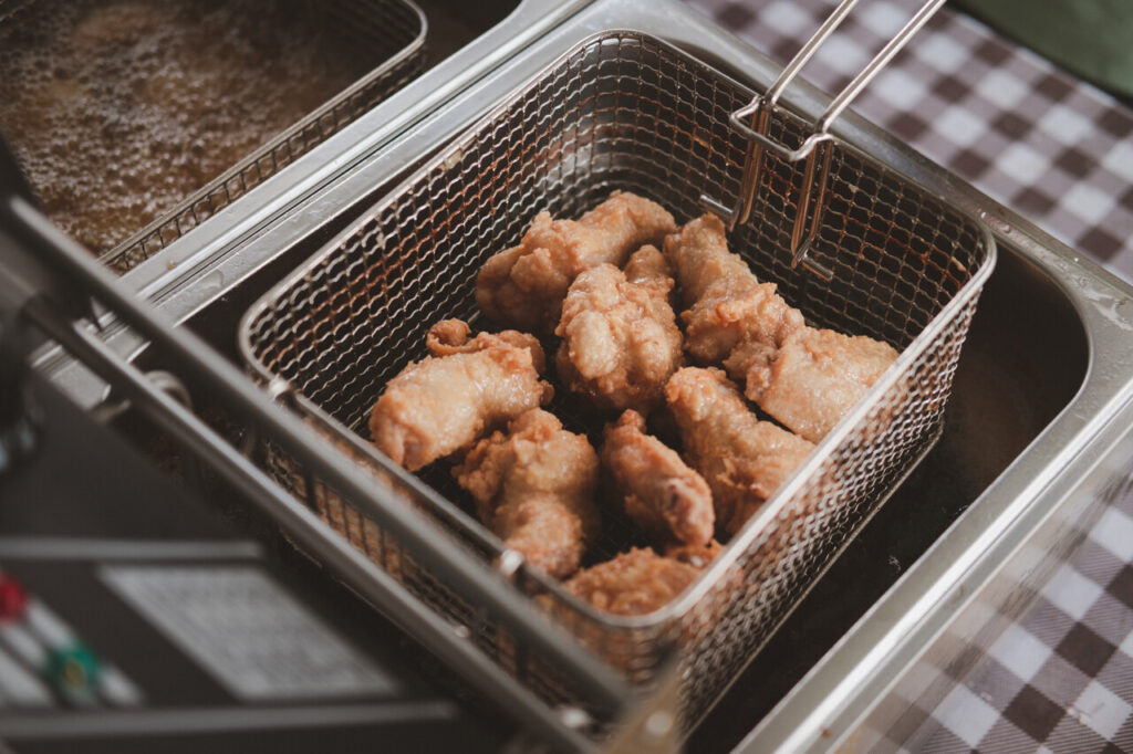 Raw chicken in a stainless steel basket ready to in the deep fryer. Close up