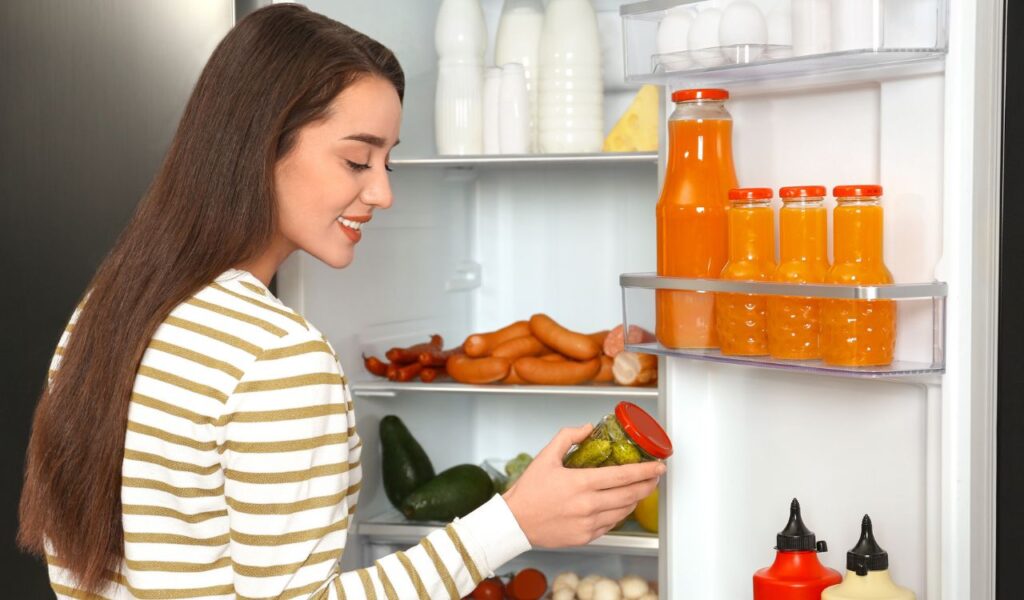 Young woman taking pickles out of fridge