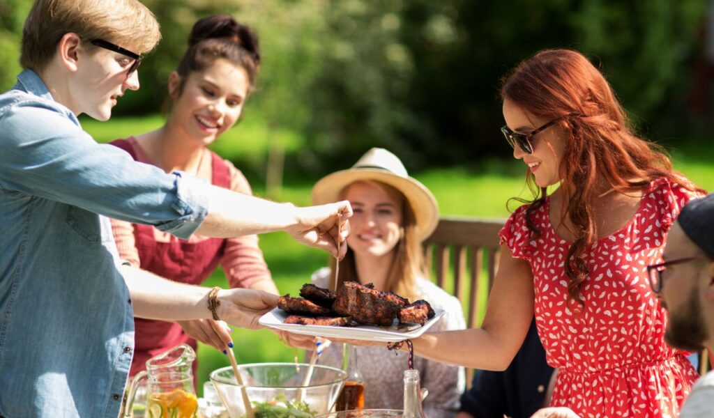 leisure, holidays, eating, people and food concept - happy friends having meat for dinner at summer garden party