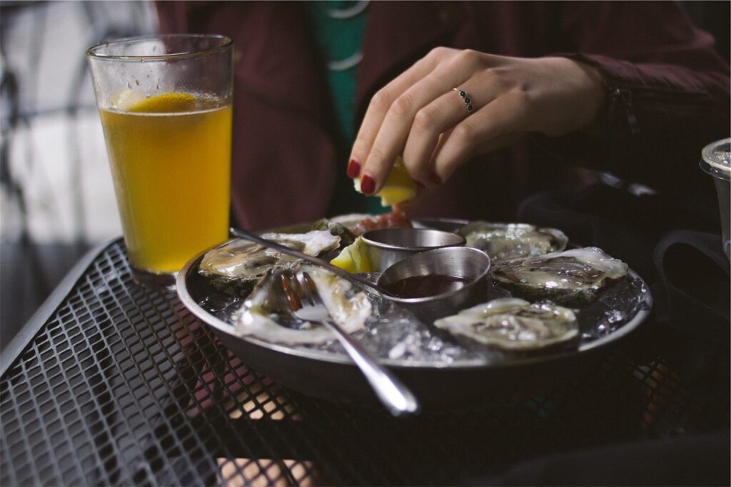 A glass of amber ale beside grilled or roasted oysters.