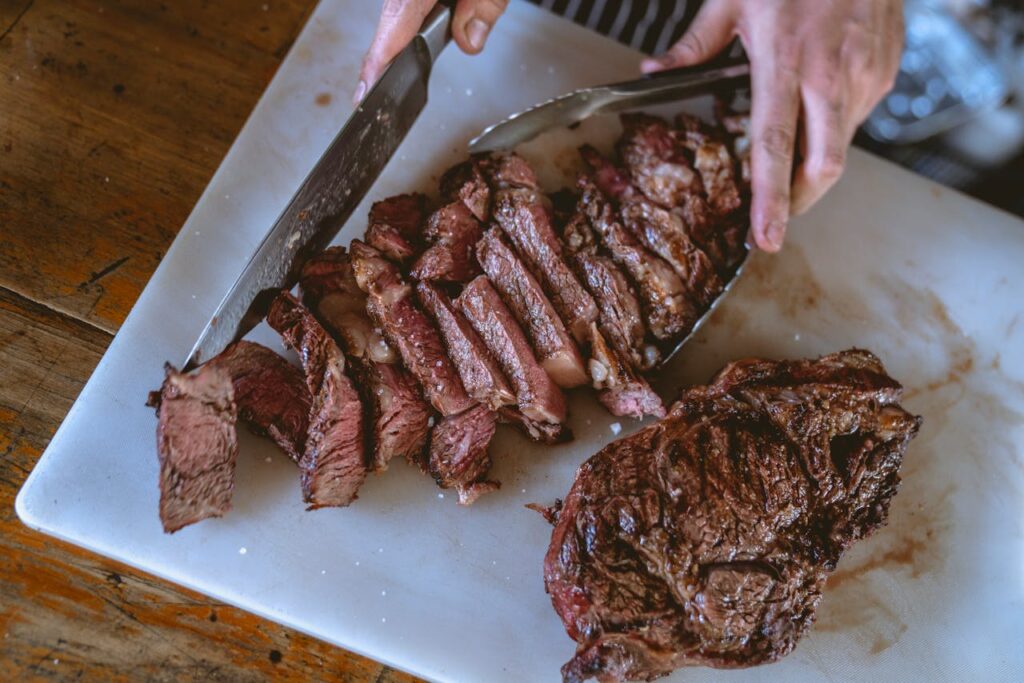 Rested steak being sliced against the grain with herb butter on top.