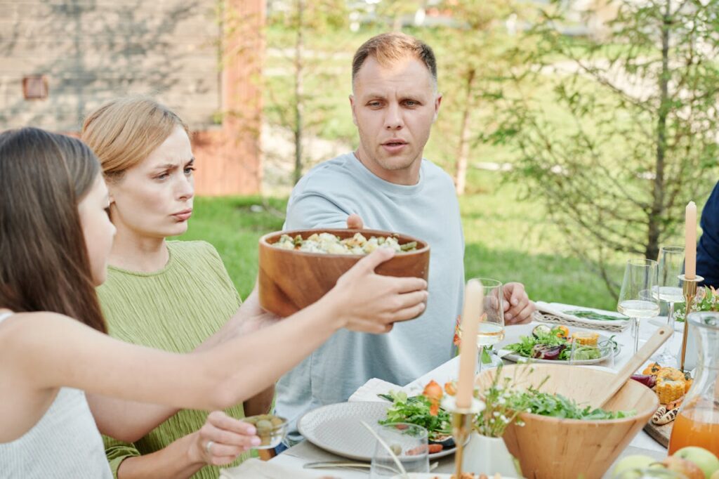 A family picnic scene with people serving potato salad from a large bowl.