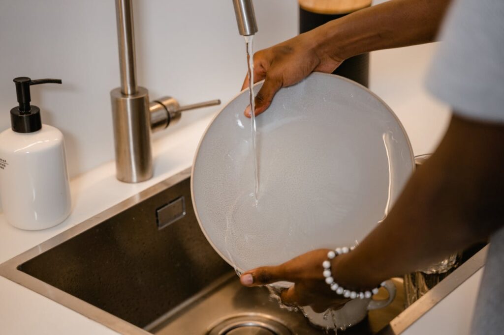 A cutting board and utensils used for raw meat being thoroughly rinsed under a running tap,