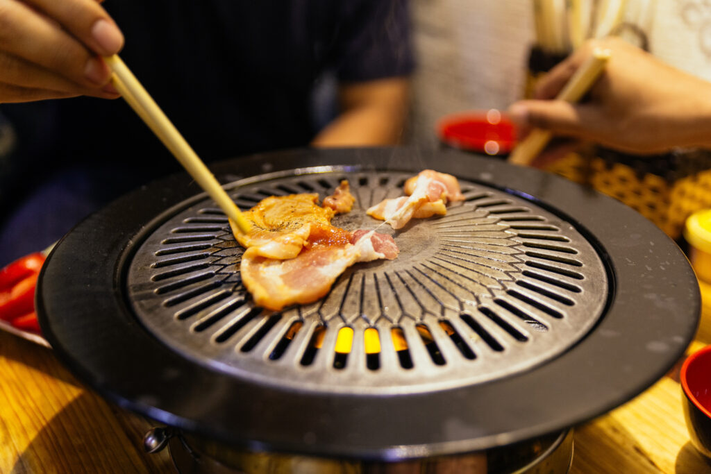 Grilling sliced BBQ pork on hot pan by chopstick at the restaurant in Hanoi, Vietnam.